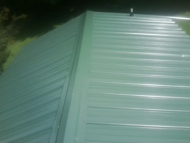 New green metal panels meeting at the ridge of a roof — Flat Roof Repair work by our crew in Paterson